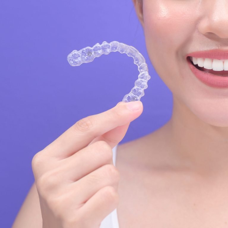 A young smiling woman holding invisalign braces in studio, dental healthcare and Orthodontic concept.