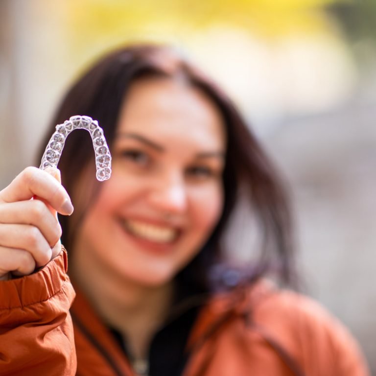 Happy young woman smiling with invisible teeth aligner during fall season at park.